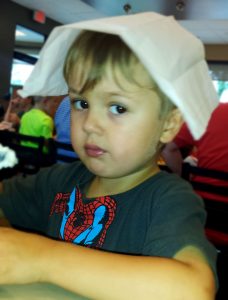 Toddler boy wearing a spider-man t-shirt has a brain freeze and has put a white paper napkin across his head.