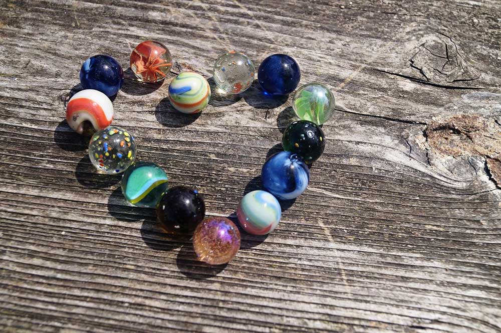 An assortment of glass marbles arranged in a heart shape on a piece of rough wood.