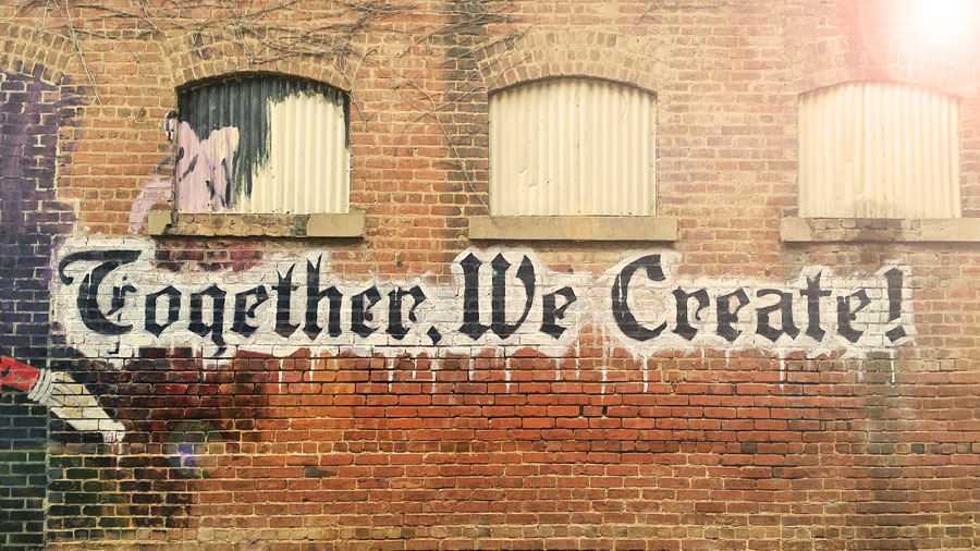 Brick Wall that has graffiti stating Together We Create