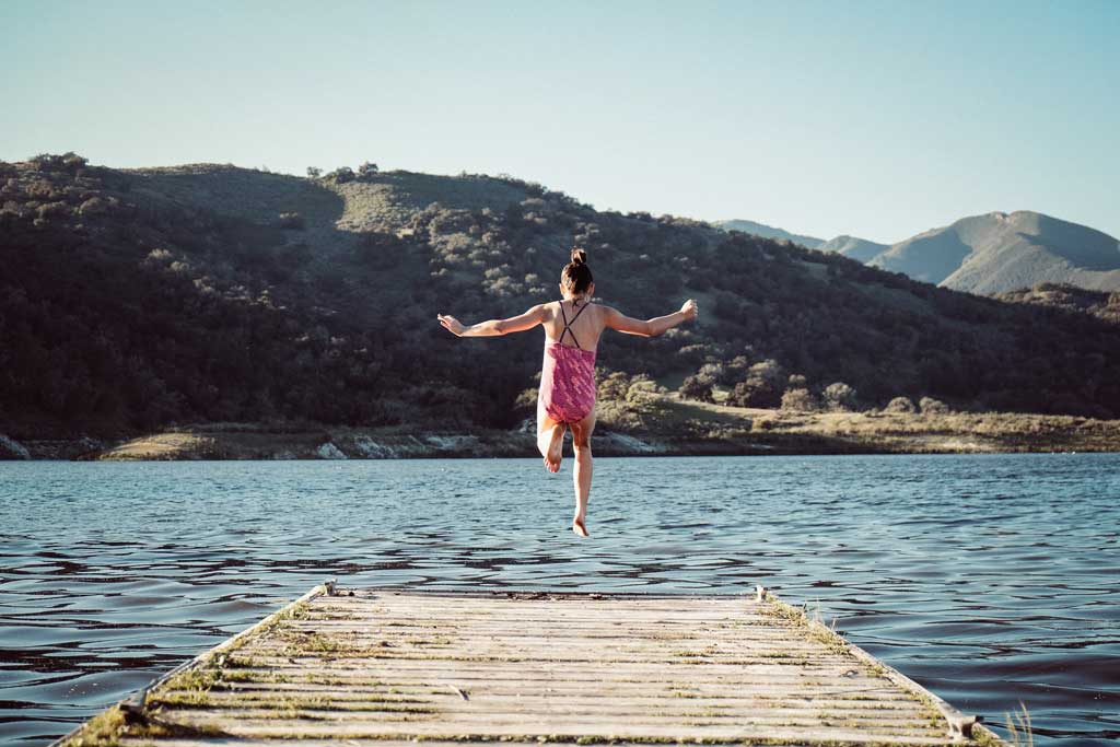 Summer overnight camp fun, girl jumping into a lake