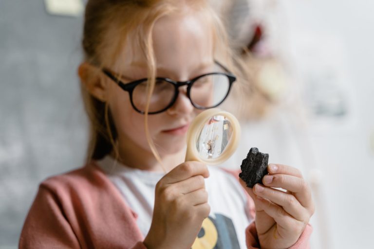 a girl looking at a rock using a magnifying glass
