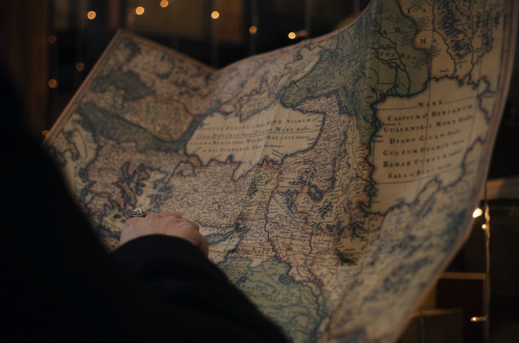 From behind anonymous person examining antique world map printed on large paper in blue colors in dark room