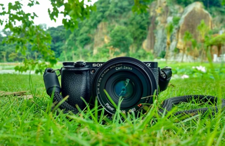 Camera with Carl Zeiss lens on grass, surrounded by nature and vibrant greenery.