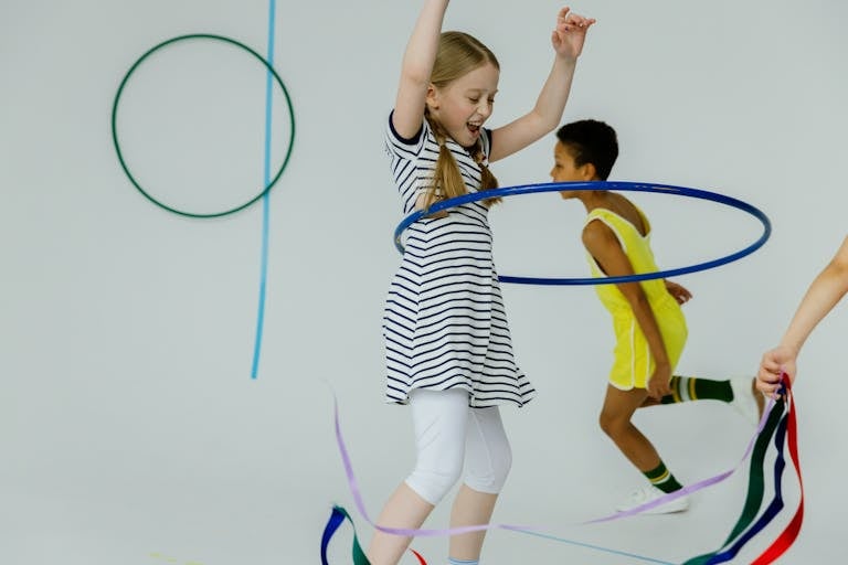 Happy children playing with hula hoops and ribbons indoors, having fun.