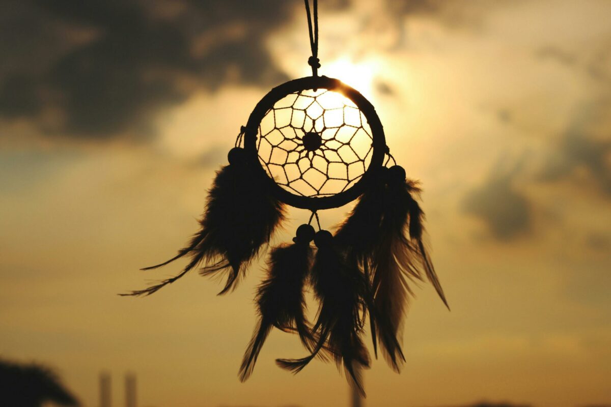 Silhouette of a dreamcatcher hanging against a serene sunset sky.