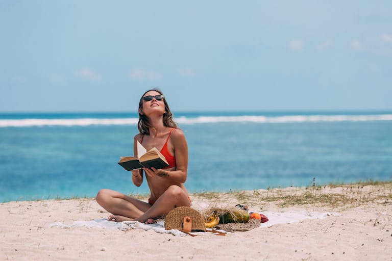 Hot List - Woman in bikini reading a book on a sunny beach, enjoying summer vacation.